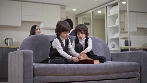 Wide Shot of Positive Friendly Siblings Sitting on Couch Reading Book Talking Smiling