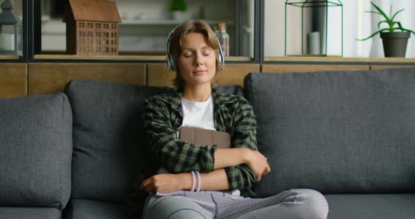 Woman with Closed Eyes Is Listening Music in Wireless Headset, Holding Gadget