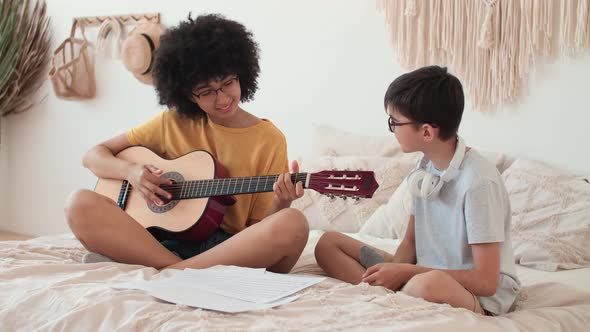 Cheerful Couple Playing Guitar While Sitting on Bed