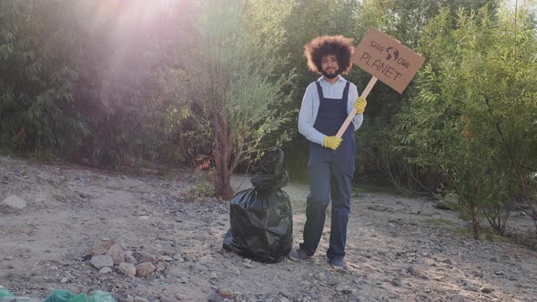 Young Activist in Work Overalls Standing with Banner Save Planet and Looking in Camera