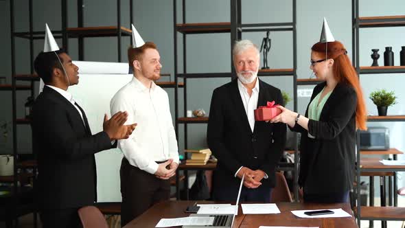 Happy Business Team of Multiethnic Businessmen Giving Present To Smiling Mature Adult Male Leader.
