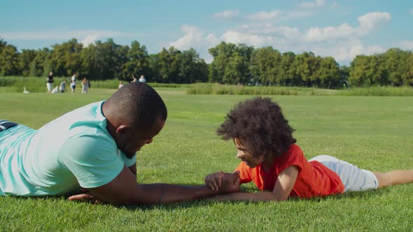 Father and Little Boy Arm Wrestling on Green Grass