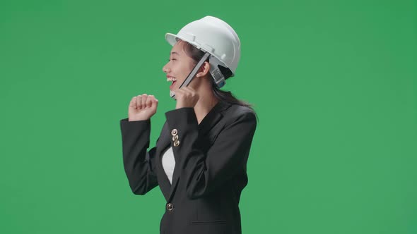 Side View Of Smiling Asian Female Engineer With Safety Helmet Dancing In The Green Screen Studio