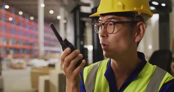 Asian male worker wearing safety suit with helmet talking in warehouse