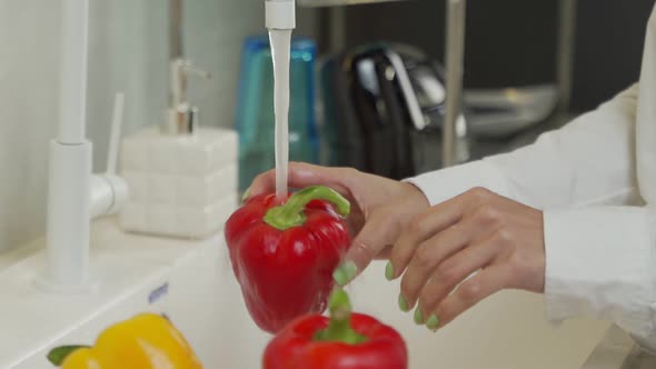 Young Woman Washes Red Pepper Under Tap Water in Kitchen