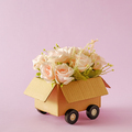 A blooming bouquet of flowers of romantic pink roses as a gift in a delivery box with truck wheels. - PhotoDune Item for Sale
