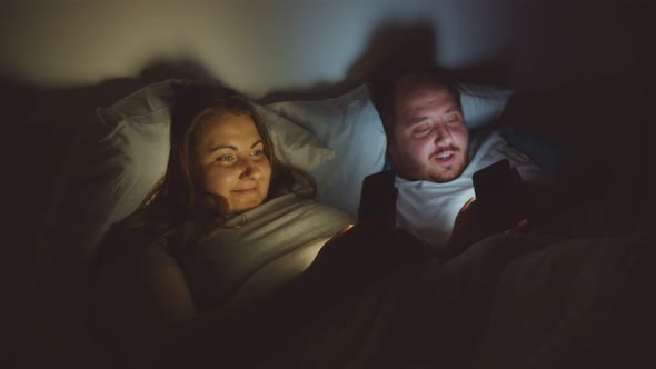 Fat Young Couple Using Smartphone Lying in Bed Together in Dark Room