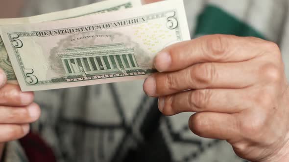 Close-up of an elderly man's hand holding a 1 and 5 American dollar bill