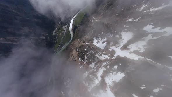 FPV drone dives down some austrian mountains with snow trough some clouds in early spring on a sunny