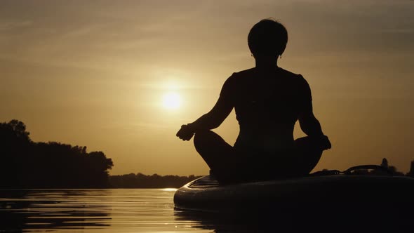 Woman Meditating on SUP Board at Sunset