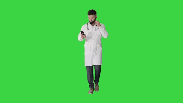 Male Doctor in White Medical Uniform Walking and Using Smartphone on a Green Screen, Chroma Key.
