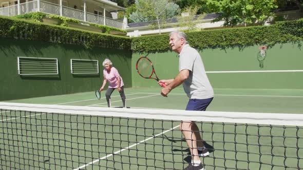 Happy caucasian senior couple playing as a doubles team at outdoor tennis court after playing a game