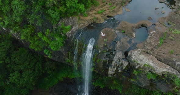 A Beautiful Woman in a White Dress on Top of a Waterfall in a Green Jungle Enjoys Her Victory
