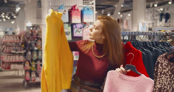 Young Lady Standing in Clothes Shop Indoors Choosing Sweater