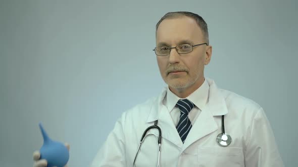 Funny Doctor Pressing on Rectal Syringe With Smile on Face, Proctologist Joking