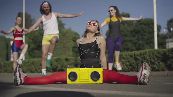 Flexible Slim Caucasian Sportswoman Sitting on Twine on Road with Vintage Yellow Tape Recorder As