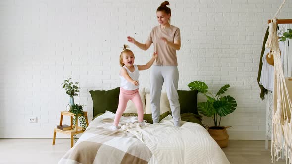 Young Mom and Child Little Daughter Jumping on the Bed