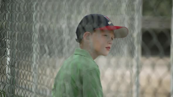 Slow motion rack focus of boy sitting in dugout behind chain link fence.