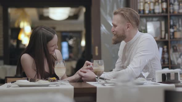 Portrait Cute Brunette Woman and a Handsome Bearded Blond Man Sitting at the Table in Front of Each