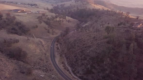 Aerial view of car driving through mountain road at golden hour