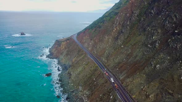 Overhead aerial view of a car driving along cliffs of the Pacific Ocean coast in Big Sur on State Ro