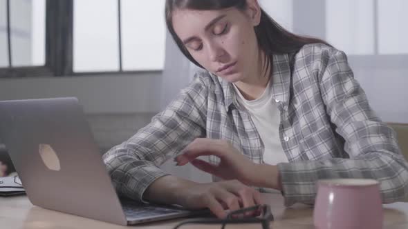 Young Caucasian Girl Taking Off Black Eyeglasses and Putting Head on Laptop Keyboard. Tired Young