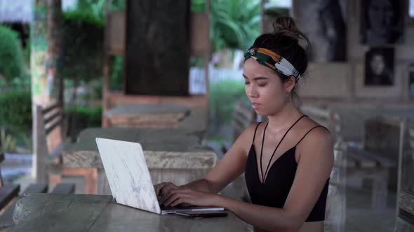 Young freelancer girl typing on laptop searching for inspiration at beach, Bali