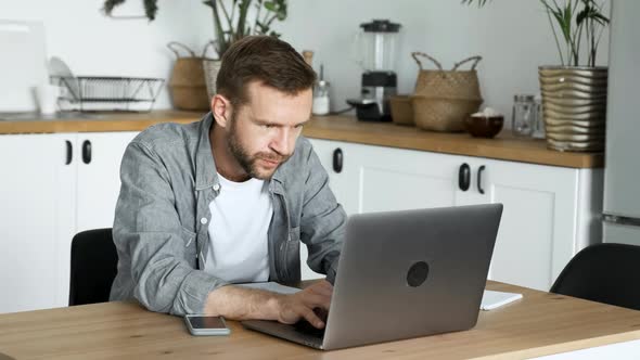 A Young Freelance Man Works At A Computer, Looks at The Monitor Screen, Is in A Room At Home