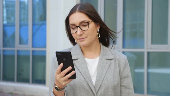 Woman in a Formal Suit and Glasses Walks and Looks at the Phone on the Street Slow Motion