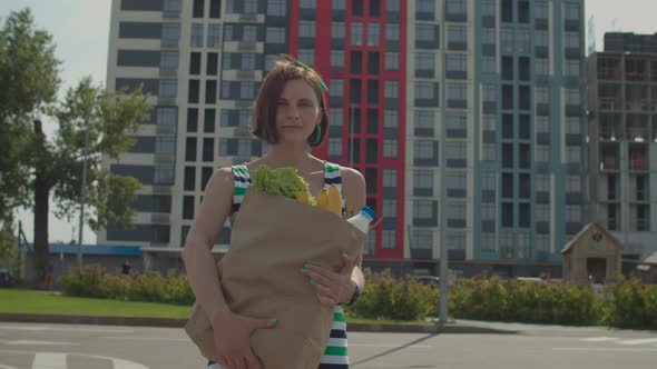 30s woman in dress walking holding big paper grocery bag in hands