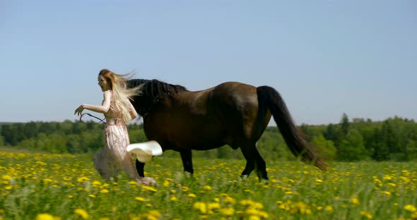 Young Blonde Woman and Brown Horse Are Running Together Over Blooming Field in Summer Day