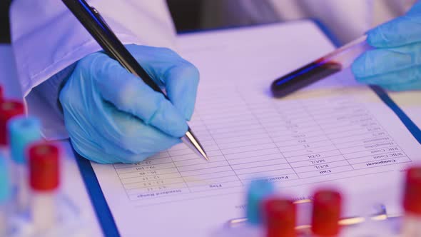 Hands of a Doctor or Laboratory Worker Making Notes About Blood Samples on Clipboard