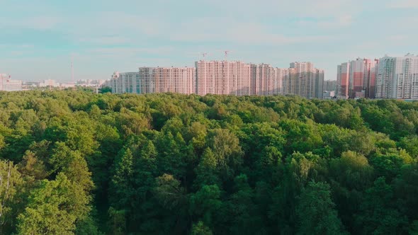 Drone Flies Over Park Towards Huge Housing Estates Under Construction at Sunset Construction Cranes