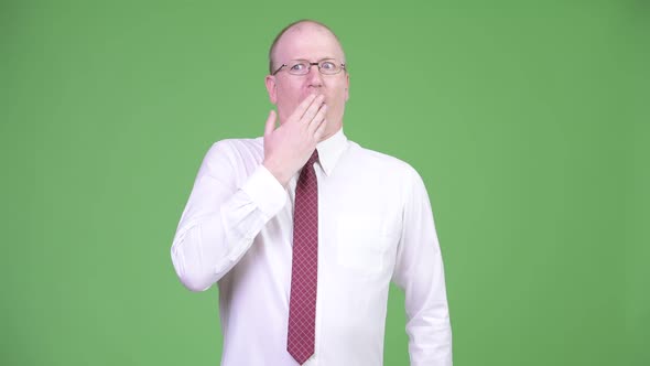 Mature Bald Businessman Covering Mouth While Looking Guilty