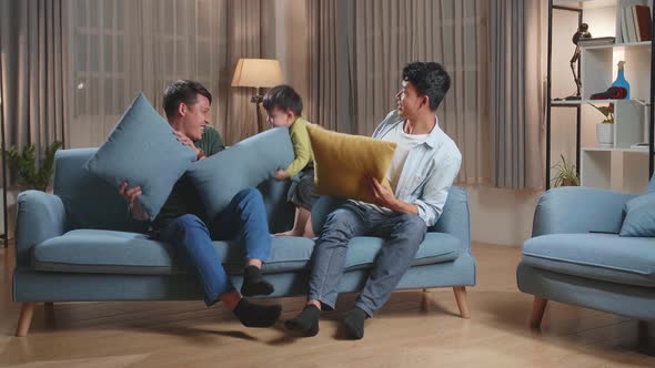 Happy Asian Gay Couple Having Fun With Their Lovely Son Fighting Pillows In Living Room