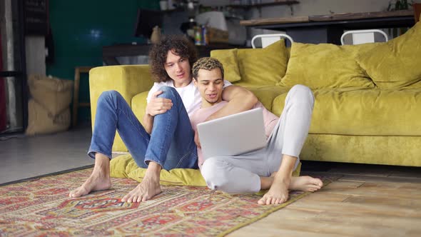 Male Romantic Gay Couple Sitting on the Floor Together Looking on Laptop Screen