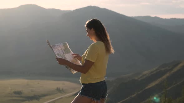 Beautiful Girl Tourist Looking a Map While Standing on the Edge of a Mountain During Sunset