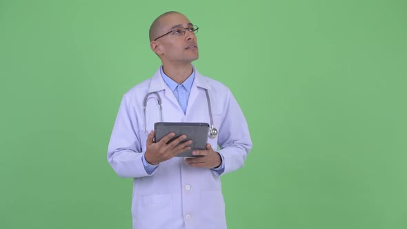 Happy Bald Multi Ethnic Man Doctor Thinking While Using Digital Tablet