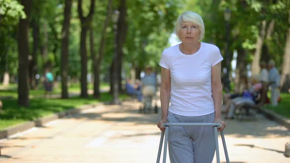 Upset Old Woman Moving Outdoors With Walking Frame, Rehabilitation After Trauma