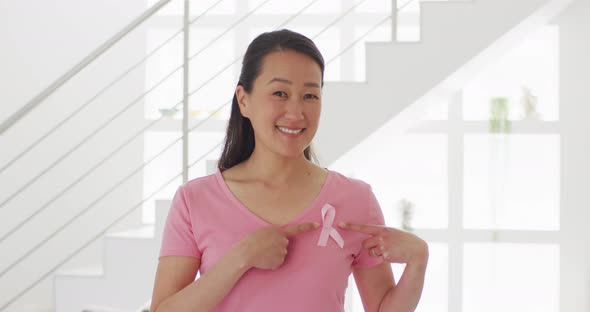 Happy asian woman in pink tshirt showing pink ribbon at home