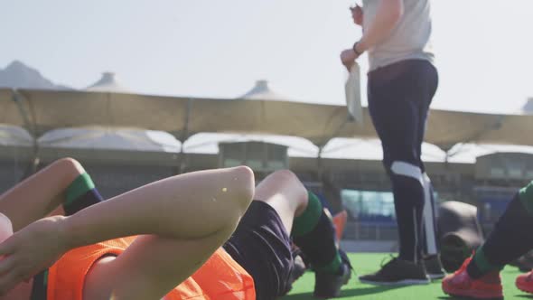 Coach watching female hockey players exercising on the field