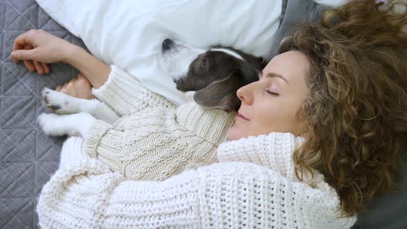 Young Woman Sleeping With Dog While Lying On Bed Wearing Cozy Knit Sweaters