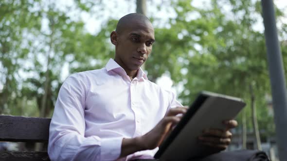 Concentrated African businessman typing by tablet