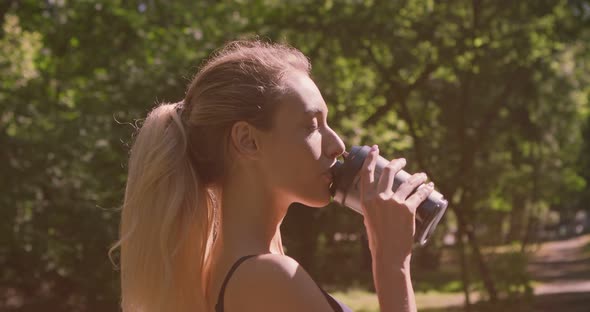 Tracking Shot of Young Sporty Girl Drinking Water Outdoor and Laughing