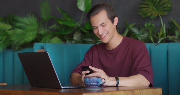Happy Man Using Phon and Laughing While Having a Cup of Coffee in Nice Cafe