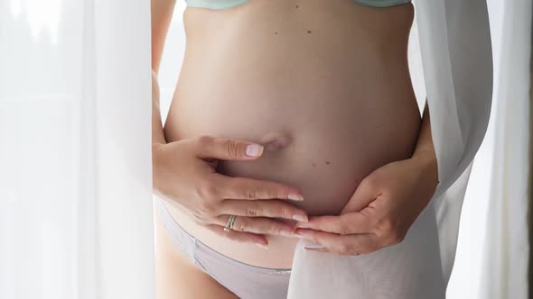 Closeup of Pregnant Woman Covering in White Fabric and Holding Her Big Growing Belly
