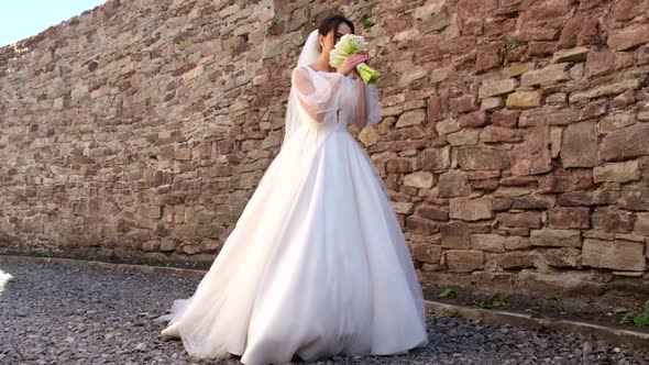 Brunette Bride in a White Wedding Dress She Carries a White Bouquet of Flowers in Her Hands