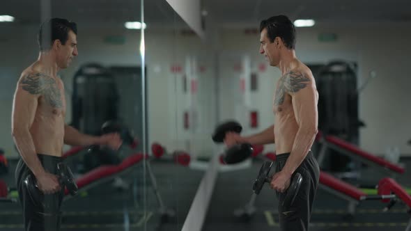 Side View Focused Sportsman Lifting Dumbbells Reflecting in Gym Mirror