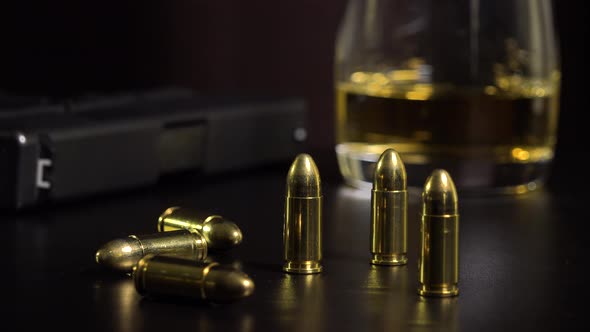 Closeup on Bullets on a Black Table - a Gun and a Glass of Whiskey in the Blurry Background