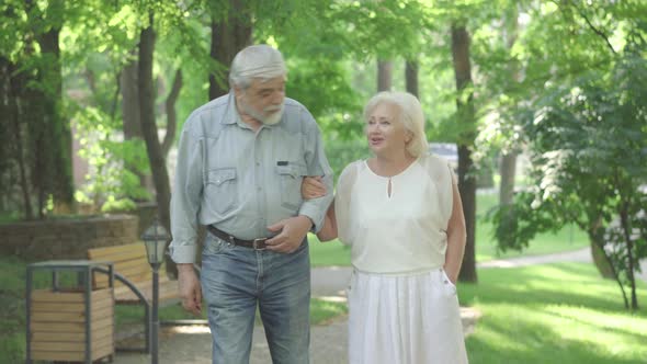 Portrait of Carefree Senior Husband and Wife Strolling in Sunny Park and Talking. Happy Old